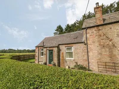 an old brick house with a green door on a hill at Waterside Lodge in Lockerbie