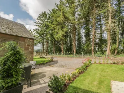 a garden with a bench and trees in the background at Waterside Lodge in Lockerbie