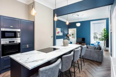 a kitchen with a bar with chairs and a living room at The Oliver in Ayr