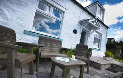 a white house with two benches and a window at Bardristane Forge in Gatehouse of Fleet