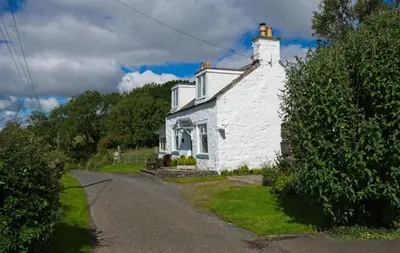 a white house with a chimney on a road at Bardristane Forge in Gatehouse of Fleet