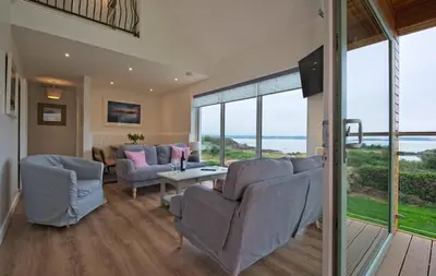 a living room with couches and a table and windows at Curlew Cottage in Gatehouse of Fleet