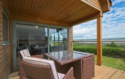a patio with a glass table and chairs on a deck at Curlew Cottage in Gatehouse of Fleet