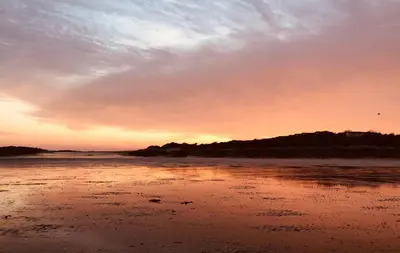 a sunset on a beach with the ocean at Curlew Cottage in Gatehouse of Fleet
