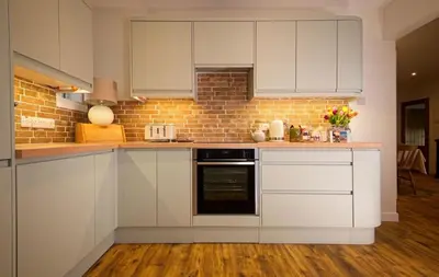 a kitchen with white cabinets and a brick wall at Edenville Cottage in Gatehouse of Fleet