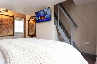 a bedroom with a white bed and a staircase at Scenery Hill Hideaways The Coach House Charming Retreat with Jacuzzi and BBQ Hut Near the Lake District in Workington