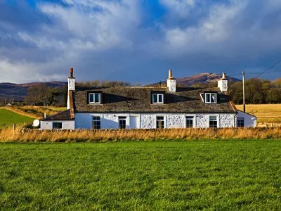 a white house with a black roof in a field at Powillimount Cottage in Dumfries