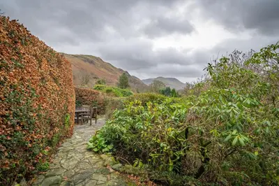 a garden with a wooden table and a fence at Ghyll Foot - At the foot of Place Fell, Ullswater in Patterdale