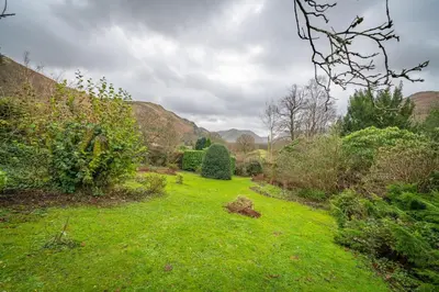 a garden with green grass and bushes on a cloudy day at Ghyll Foot - At the foot of Place Fell, Ullswater in Patterdale
