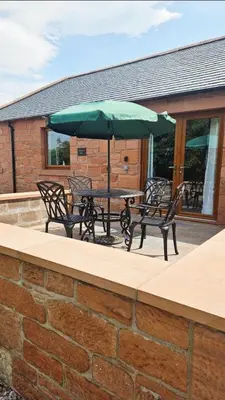a patio with two chairs and a table with an umbrella at Cosy wee cottage -modern, open plan, parking, EV in Glencaple