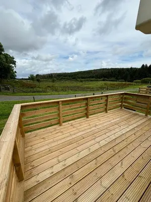 a wooden deck with a fence and a field at 131 Loch View Three Lochs Holiday Park in Newton Stewart