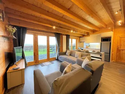 a living room with a couch and a tv and some windows at Beautiful Countryside Lodge with Outstanding Views - Pass the Keys in Dumfries