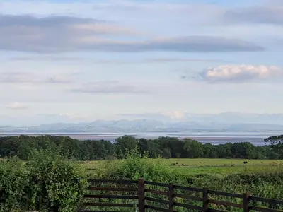 a field with a fence and a view of the water at Beautiful Countryside Lodge with Outstanding Views - Pass the Keys in Dumfries