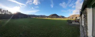 a large green field with mountains in the background at Holly Cottage Grasmere in Grasmere