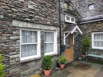 a stone house with white windows and a wooden door at Holly Cottage Grasmere in Grasmere