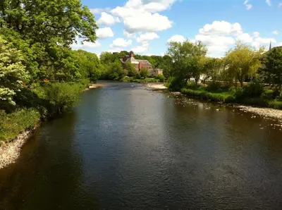 a river with trees and a house in the background at Manor House Hotel, Cockermouth in Cockermouth