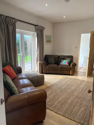 a living room with a leather couch and a window at Mains of Greenlaw Cottage in Castle Douglas