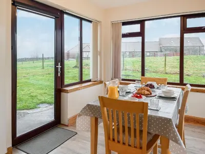 a dining room with a table and chairs and windows at Shellhill Cottage in Kirkcudbright