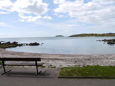 a bench sitting on a beach near the water at Albany Cottage in Rockcliffe