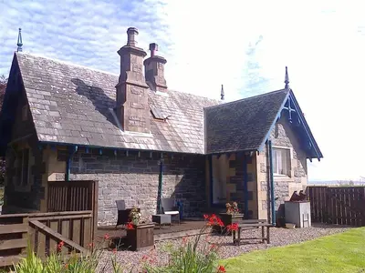 an old stone house with a wooden fence in a yard at Ardwell House East Lodge in Stranraer