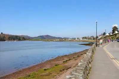 people walking along a sidewalk next to a body of water at Allonby Cottage in Kippford