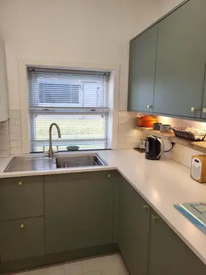 a kitchen with green cabinets and a sink and a window at The Wee House -Coorie Doon Stays in Troon