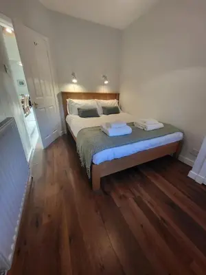 a bedroom with a large bed with wooden floors at The Wee House -Coorie Doon Stays in Troon