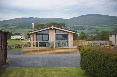 a large wooden cabin with mountains in the background at Bluebell Lodge in Girthon