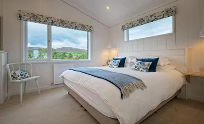 a bedroom with a large bed and two windows at Bluebell Lodge in Girthon