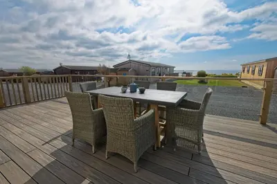 a patio with a table and chairs on a deck at Bluebell Lodge in Girthon