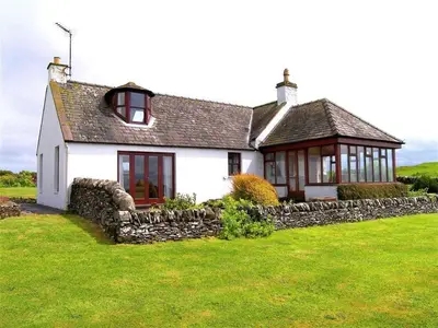 a white house with a stone wall in the yard at Allanhead Cottage in Kirkcudbright