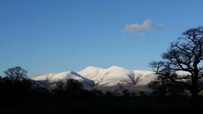 a snow covered mountain with trees in the foreground at Lake District, Mountain Views, Accessible Studio Bothy in Borrowdale Valley