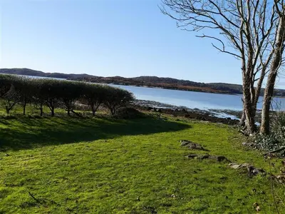 a grassy field with trees and a body of water at Calluna Cottage in Rockcliffe