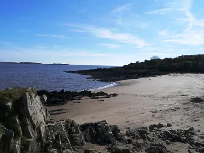 a beach with rocks and the ocean on a sunny day at Clover Lodge in Gatehouse of Fleet