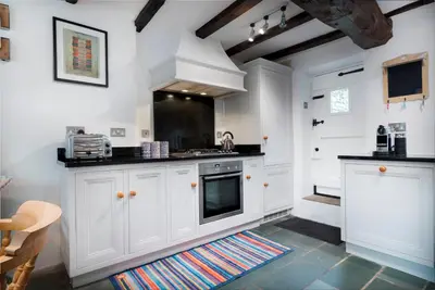 a kitchen with white cabinets and black counter tops at Bridge End Cottage Elterwater in Ambleside