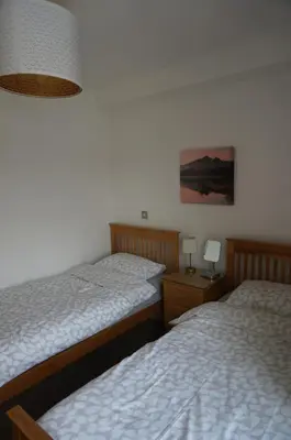 two twin beds in a bedroom with a lamp at Chaucer View, Chaucer House Apts in Keswick