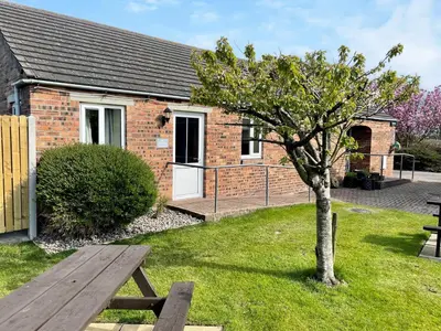 a picnic table and a tree in front of a building at Milking Parlour - Uk48911 in Allonby