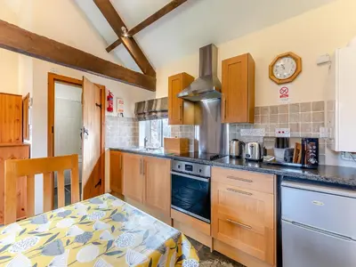 a kitchen with wooden cabinets and a table and a clock at Eight Byre - Uk48913 in Allonby