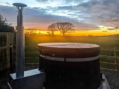 a barrel sitting next to a fence with a sunset at Meadows View Shepherd's Hut in Cockermouth
