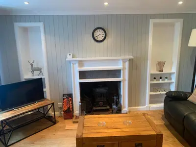 a living room with a fireplace and a clock on the wall at Campbell Cottage in Biggar