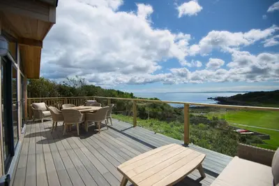 a deck with a table and chairs and a view of the ocean at Muir Lodge in Gatehouse of Fleet