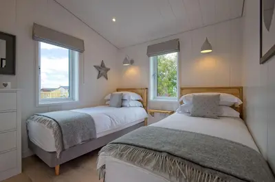 two beds in a bedroom with two windows at Muir Lodge in Gatehouse of Fleet