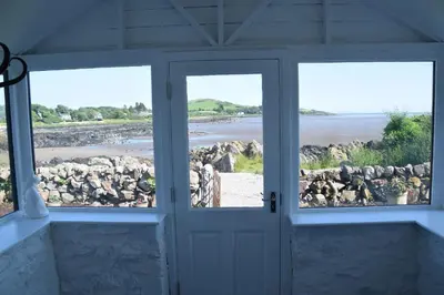 a room with a door and windows looking out at the water at Munro Cottage in Rockcliffe