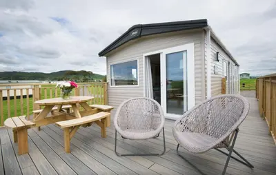 a wooden deck with a picnic table and two chairs at Pebbles in Girthon