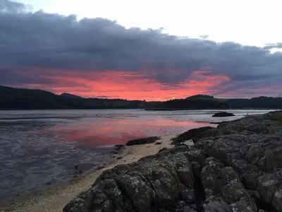 a sunset over a river with rocks in the water at Rocklea in Kippford