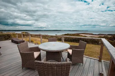 a table and chairs on a deck with a view of the ocean at The Buoys in Girthon
