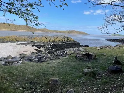 a beach with rocks and a body of water at Gardeners Cottage in Auchencairn
