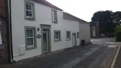 a white building with green doors on a street at Victoria Cottage in Whitrigg