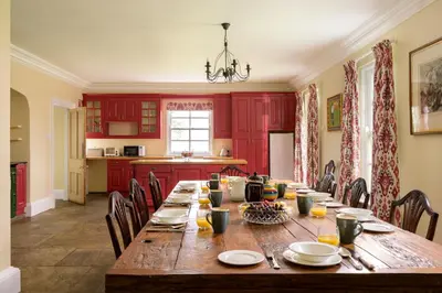 a dining room with a long table and red cabinets at Auchengashell in Kirkcudbright