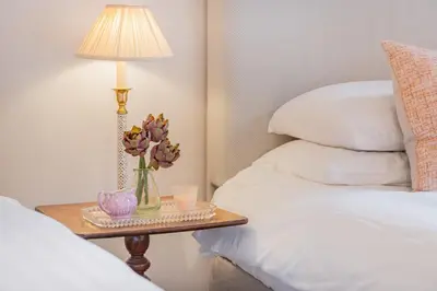 a table with a lamp and flowers on a table between two beds at Huntingstile South in Ambleside